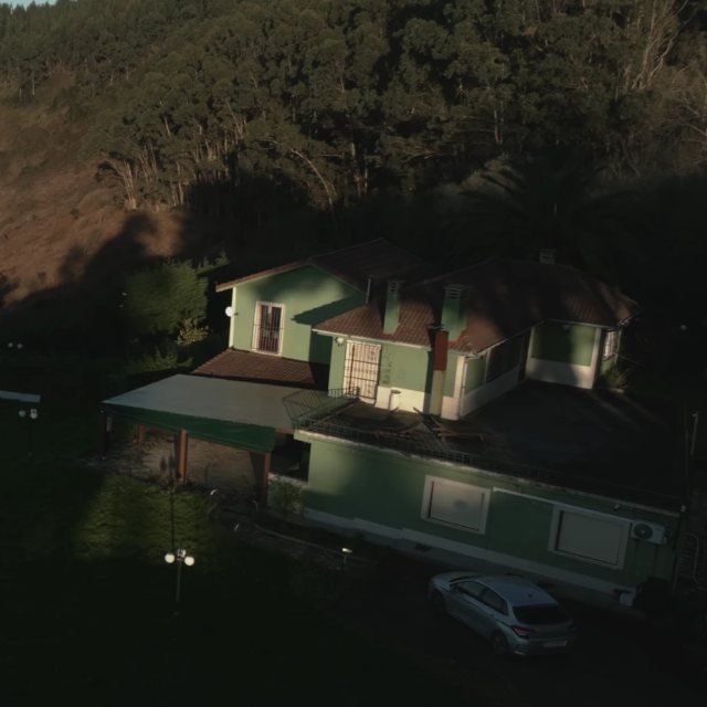 The house: a green two-storey home on the hillside, with the woods behind